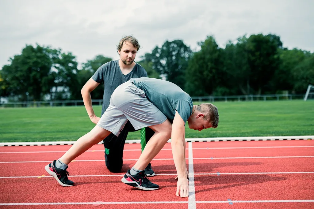 Patrick Holz kniet neben einem Läufer und korrigiert dessen Startposition auf der Laufbahn