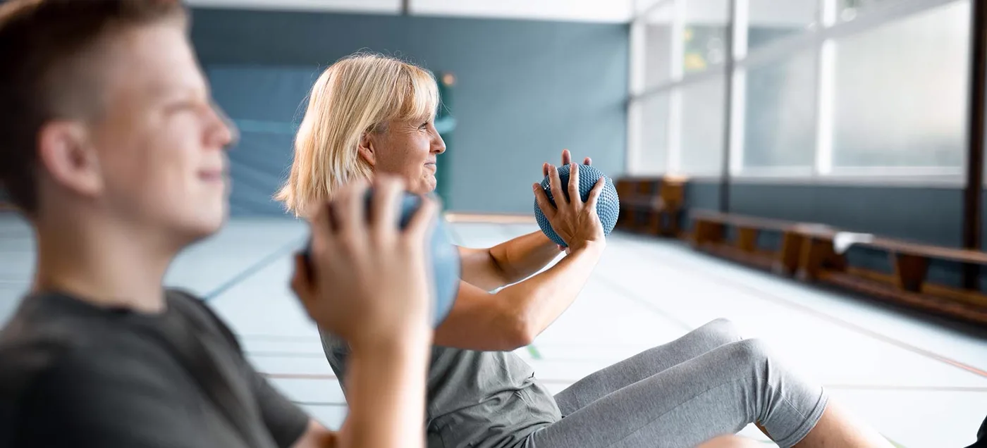 Zwei Teilnehmer trainieren gemeinsam mit dem Medizinball in der Halle